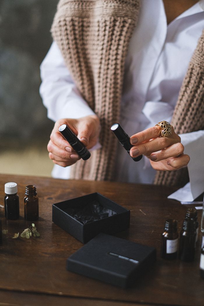 Person holding two black cosmetic bottles with small vials on a wooden table.